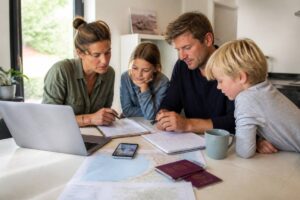 Gezin dat vakanties vergelijkt op een laptop met reisnotities op tafel